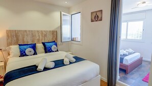 Une chambre d’hôtel moderne avec un grand lit, une tête de lit en bois et une vue sur un balcon accessible par une porte coulissante.