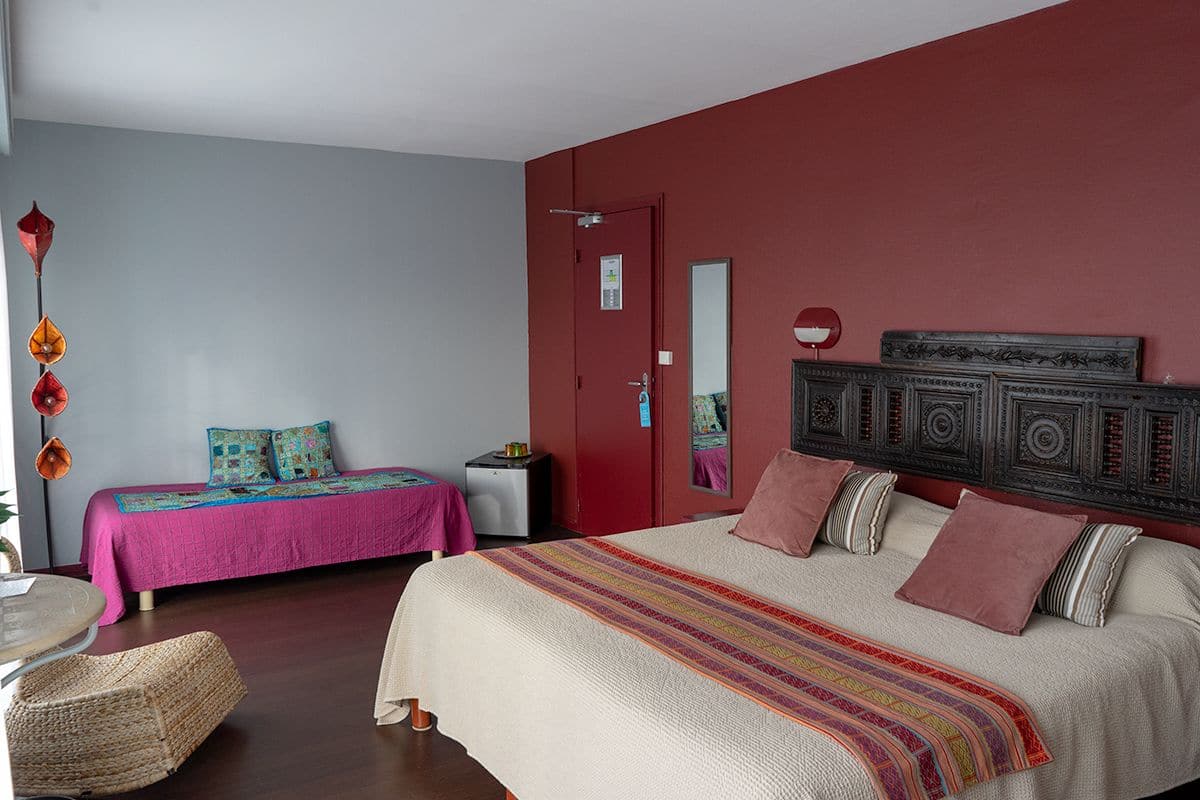 A bedroom with a large bed, a smaller bed, a red door, a mirror, and a decorative wall panel.