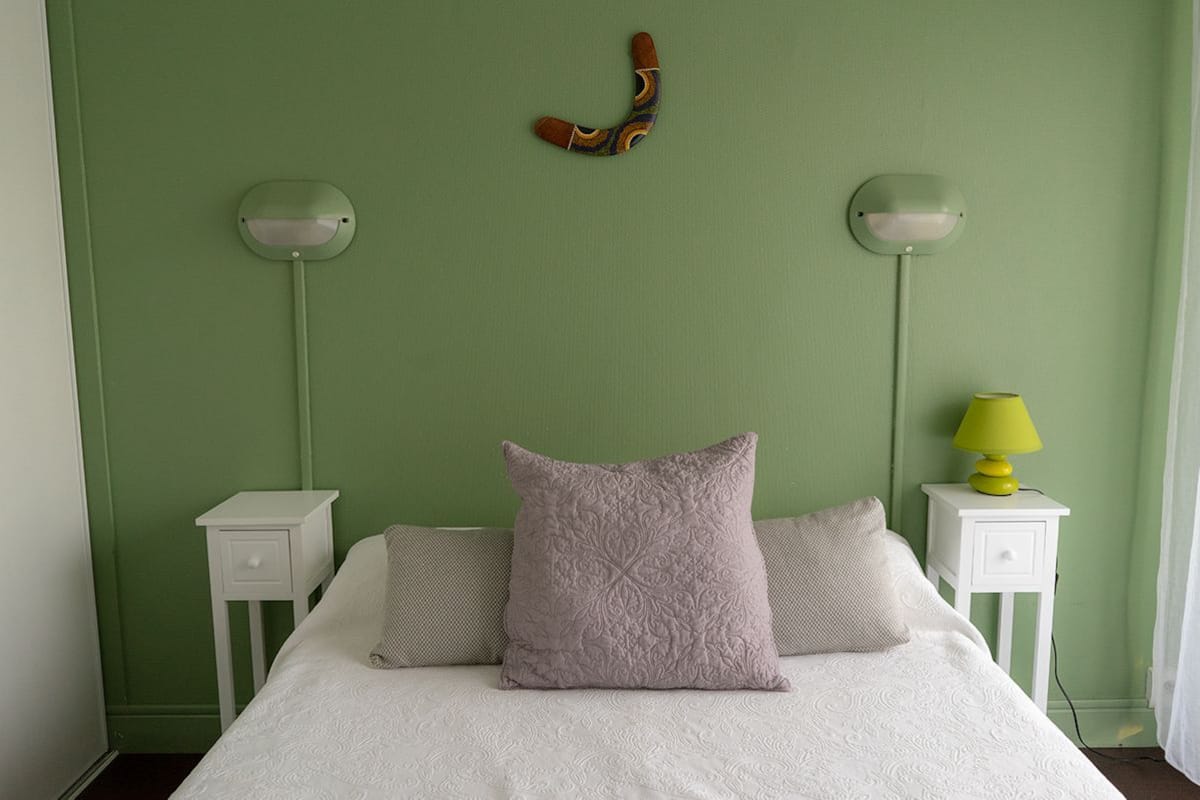 A bedroom with a green wall, a white bed, two bedside tables, and a lamp on the right table.