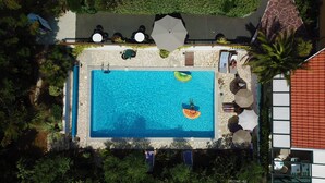 Vista aérea de una piscina con borde de piedra, rodeada de sillas de descanso y sombrillas.