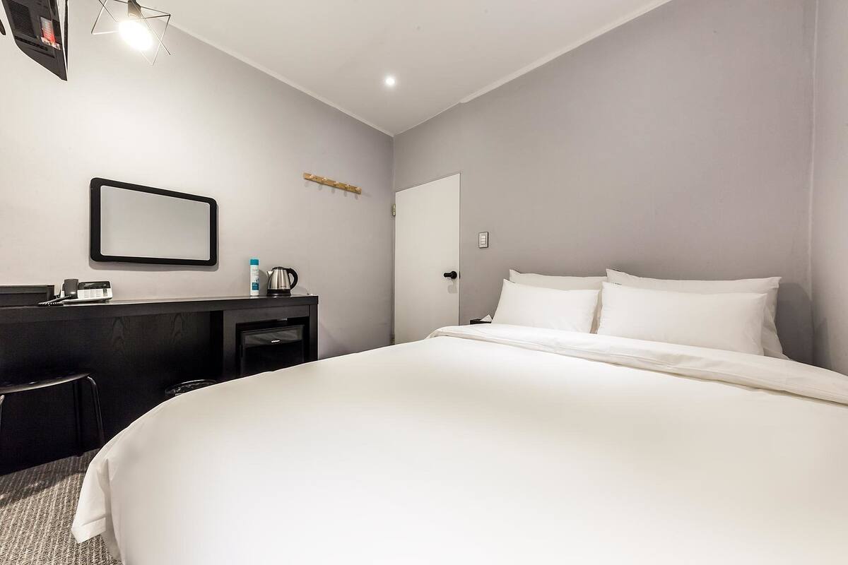 Una camera d'albergo con un letto grande, una scrivania con un telefono, un piccolo tavolino con un bollitore e una porta.