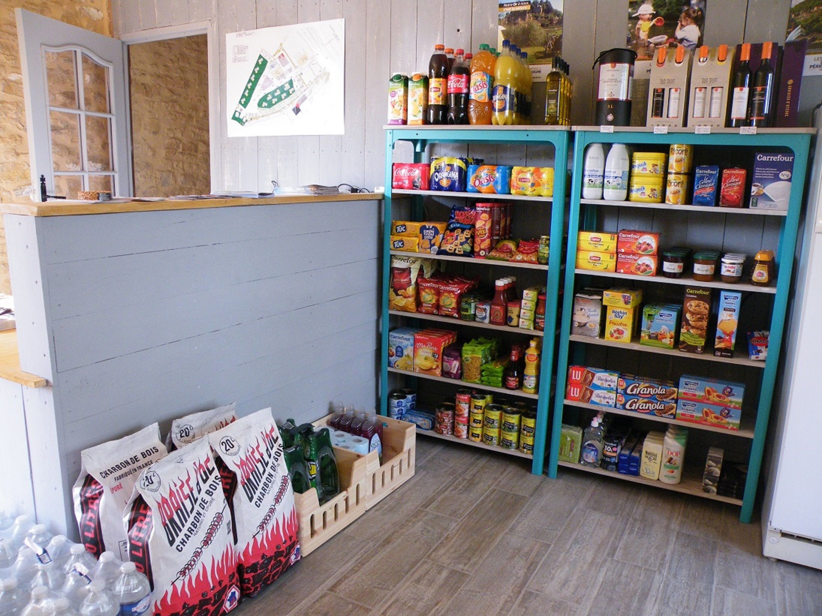 A grocery store interior with shelves stocked with various food items and beverages, a wooden counter, and a map on the wall.