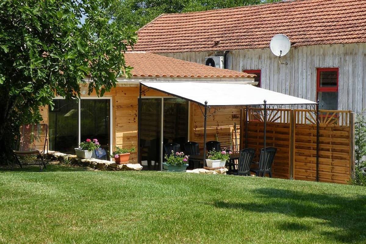 A wooden house with a red-tiled roof, a covered patio with chairs, and a satellite dish.