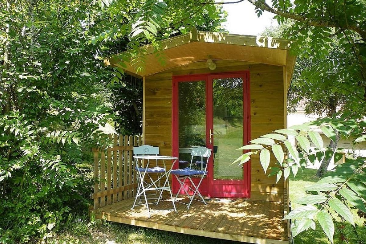 A small wooden structure with a red door and two chairs outside.