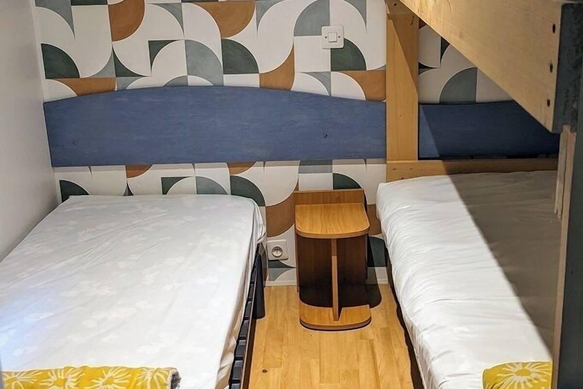 A bunk bed room with a patterned wall, a small wooden stool, and a wooden floor.