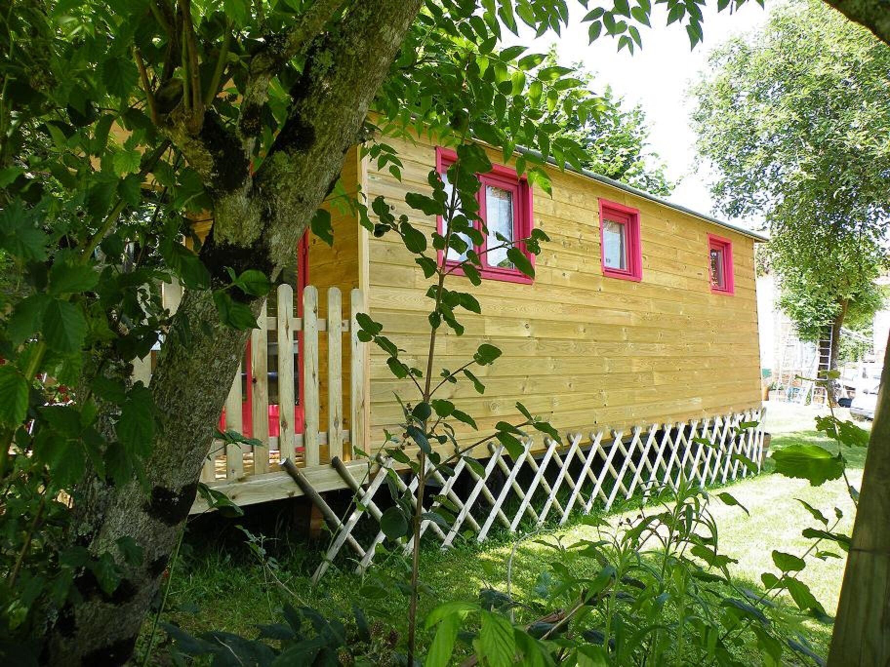 Una cabaña de madera con cerca de piquetes blancos, rodeada de follaje.