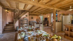 A rustic kitchen with wooden beams, a dining table set with dishes, and a staircase leading to another room. - Le Domaine de Pecany (Le Buisson-de-Cadouin)