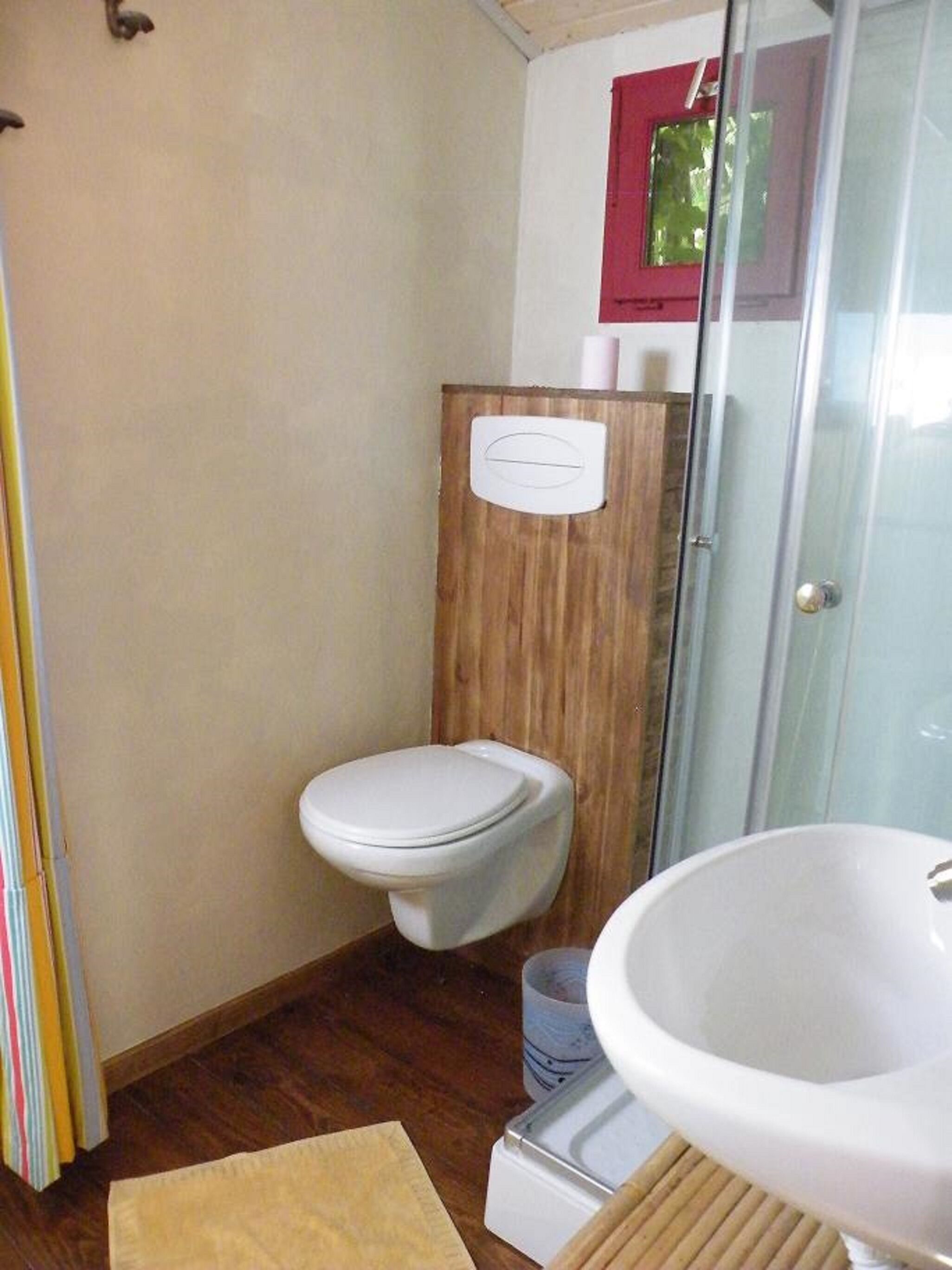 Een badkamer met een wand van houten panelen, een wit toilet, een douchecabine van glas en een witte wastafel.