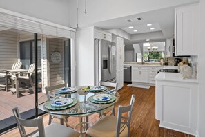 Una cocina moderna con armarios blancos, una mesa de comedor de vidrio y vistas al exterior.