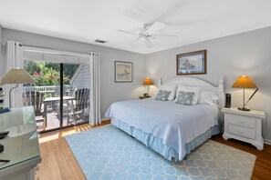 Un dormitorio con cama, dos mesitas de noche, ventilador de techo, ventana con cortinas y vistas al exterior.