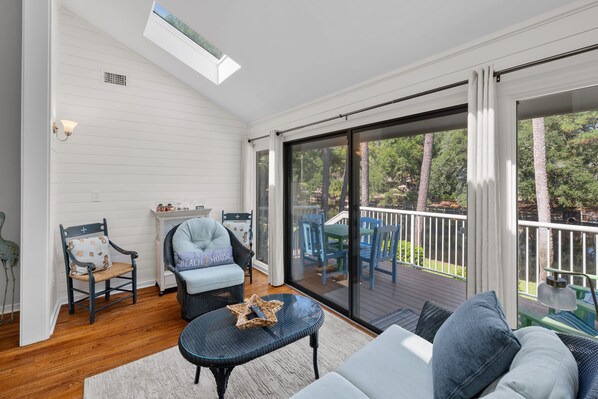 A sunlit room with a sliding glass door leading to an outdoor deck.
