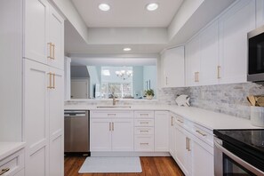 A modern kitchen with white cabinetry, gold handles, a marble backsplash, and a built-in oven.