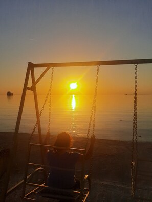 A swing set on a beach with a sunset in the background. - Mertur Hotel (Ciftlikkoy)