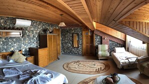 Un dormitorio acogedor y rústico con techo inclinado, vigas de madera, pared de piedra, cama con cabecera a juego, un pequeño sofá y una ventana con vistas.