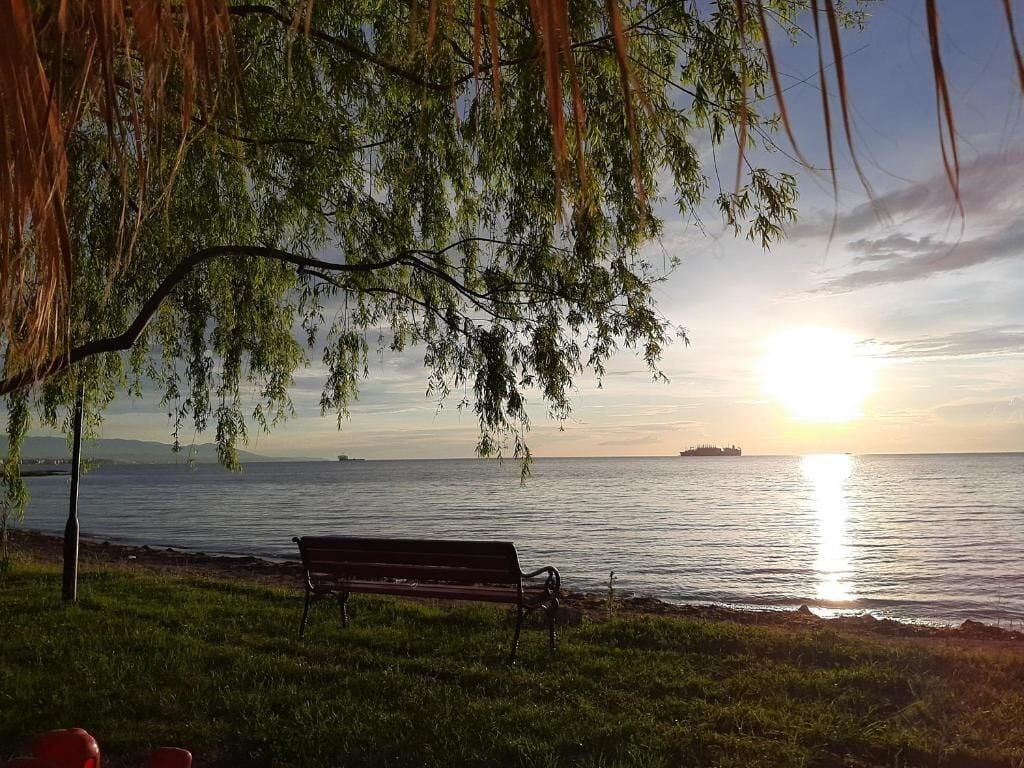 Un banco junto a un cuerpo de agua con un atardecer de fondo.