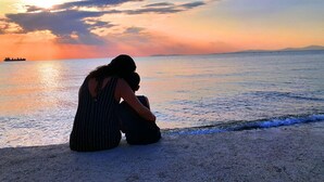 Una mujer sentada en la playa al atardecer, con un barco en la distancia.