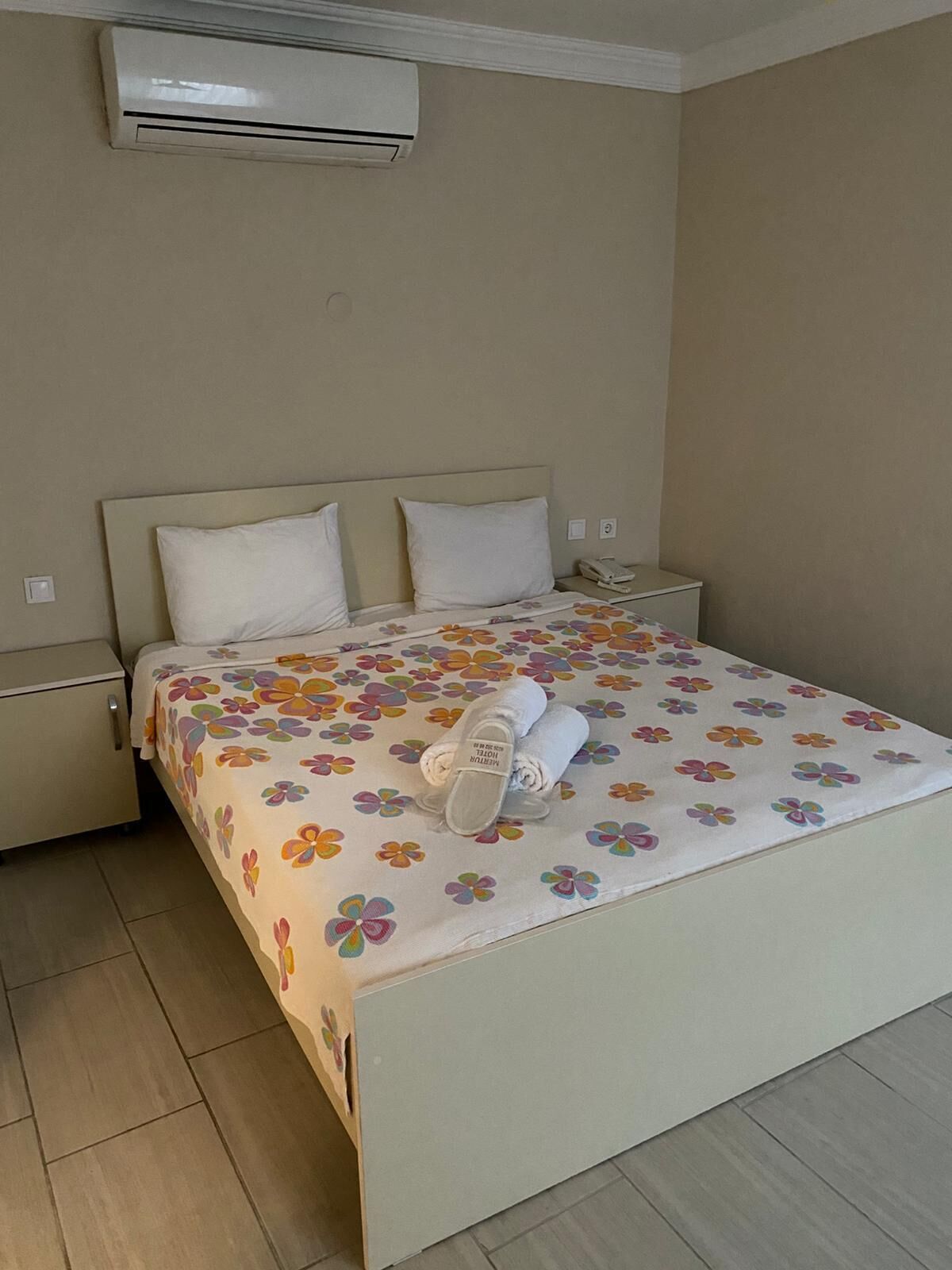 A hotel room with a bed, a nightstand, an air conditioning unit, and a telephone.