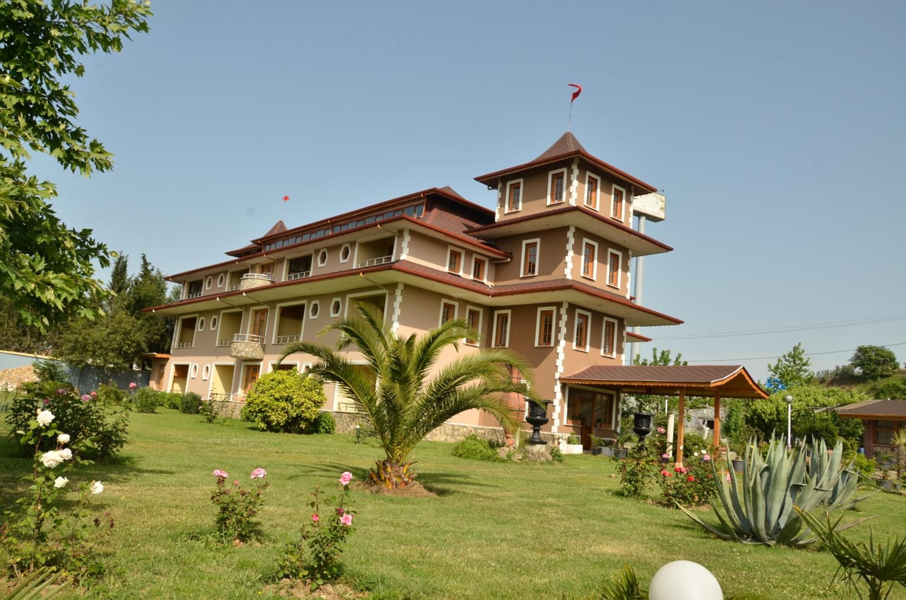 A multi-story building with a balcony, surrounded by a well-maintained garden with various plants and flowers.