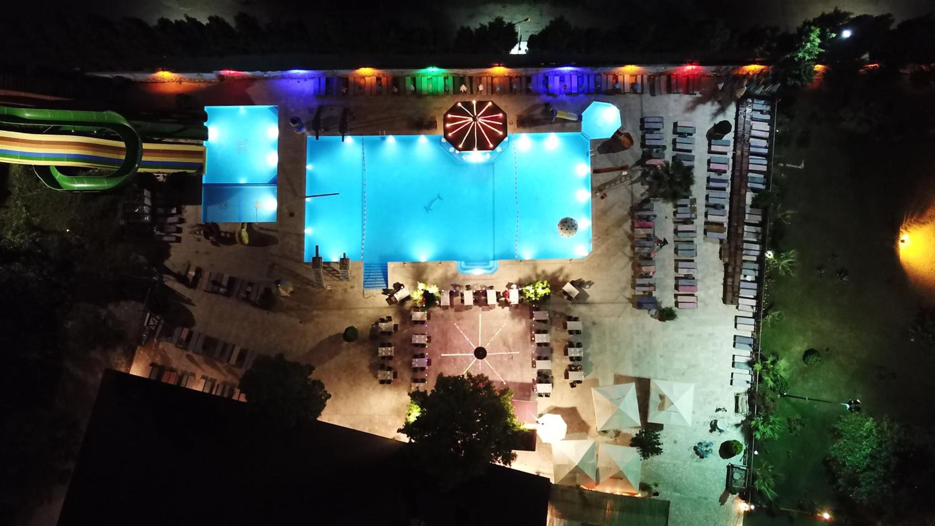 Vista aérea de un hotel con piscina, mobiliario exterior y una gran estructura iluminada.