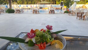 A dining table with a plate of salad and decorative flowers. - Mertur Hotel (Ciftlikkoy)