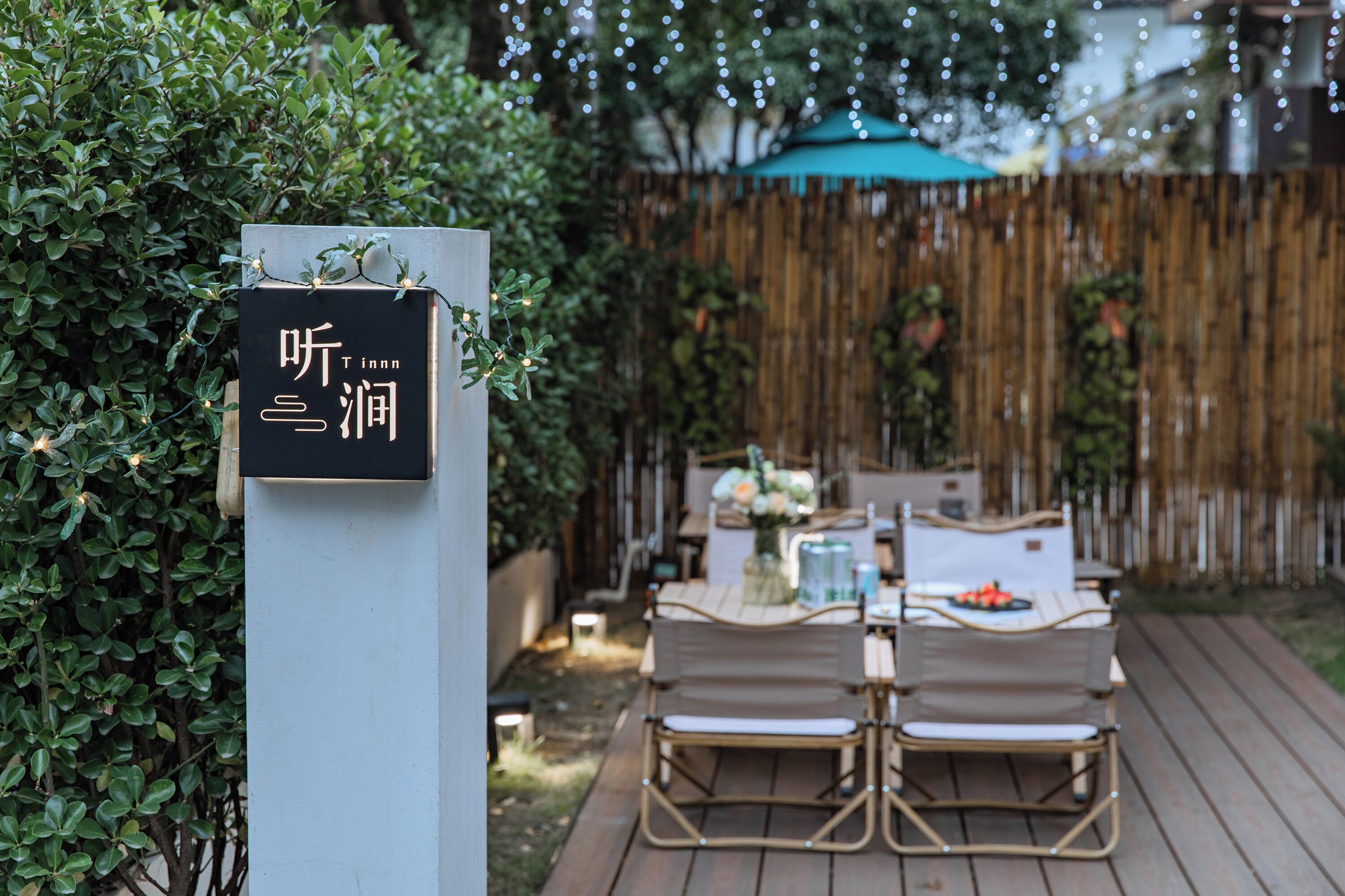 A wooden deck with a table and chairs, surrounded by greenery and a bamboo fence.