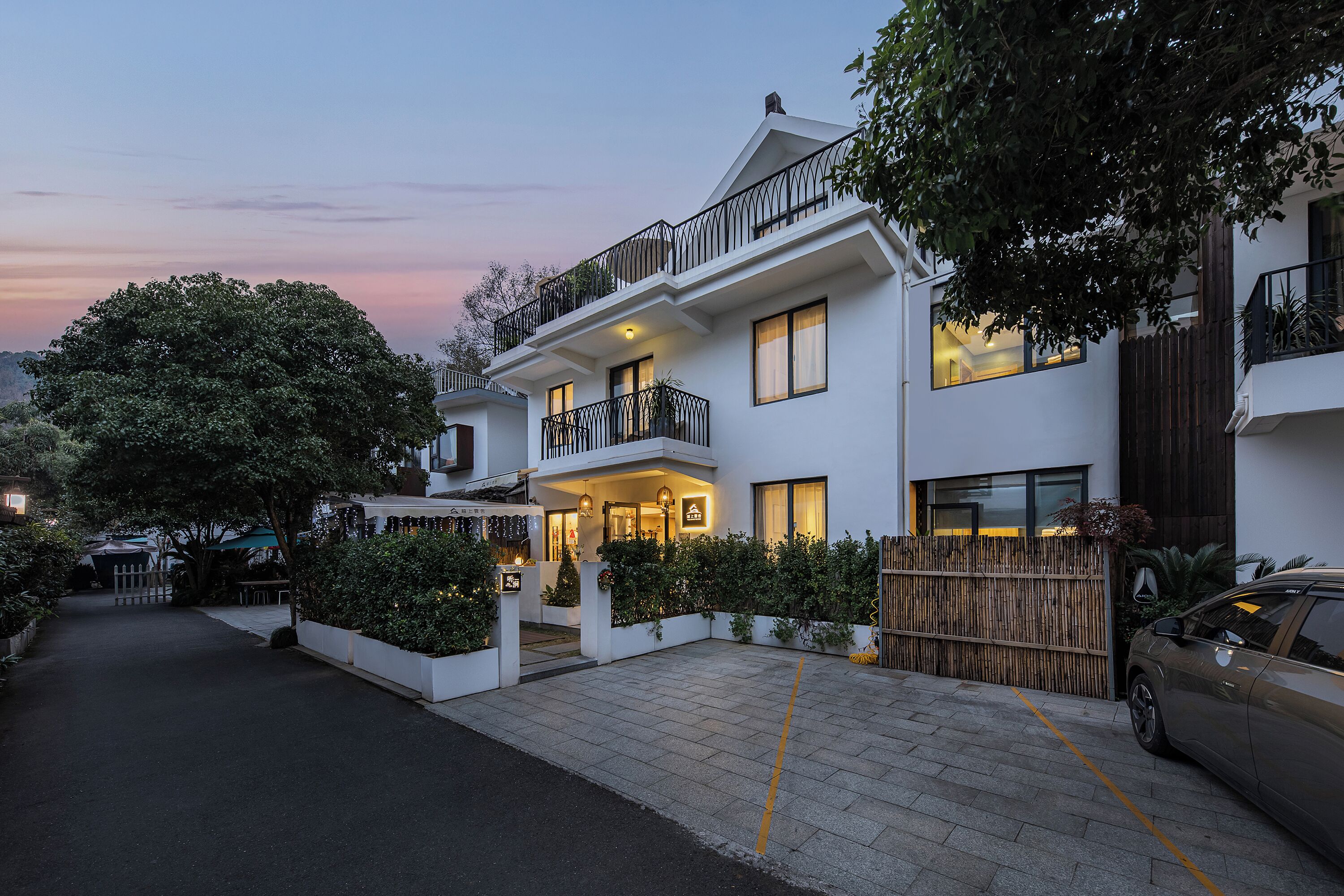 A modern two-story house with a balcony, a driveway, and a parked car.
