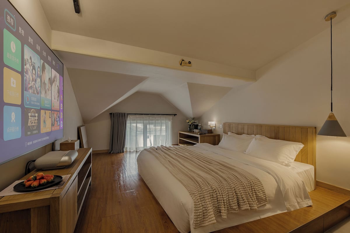 Ein modernes Hotelzimmer mit einem großen Bett, einem Holzkopfschild, einem Schreibtisch mit einem Laptop und einem Fernseher, der eine Speisekarte zeigt.