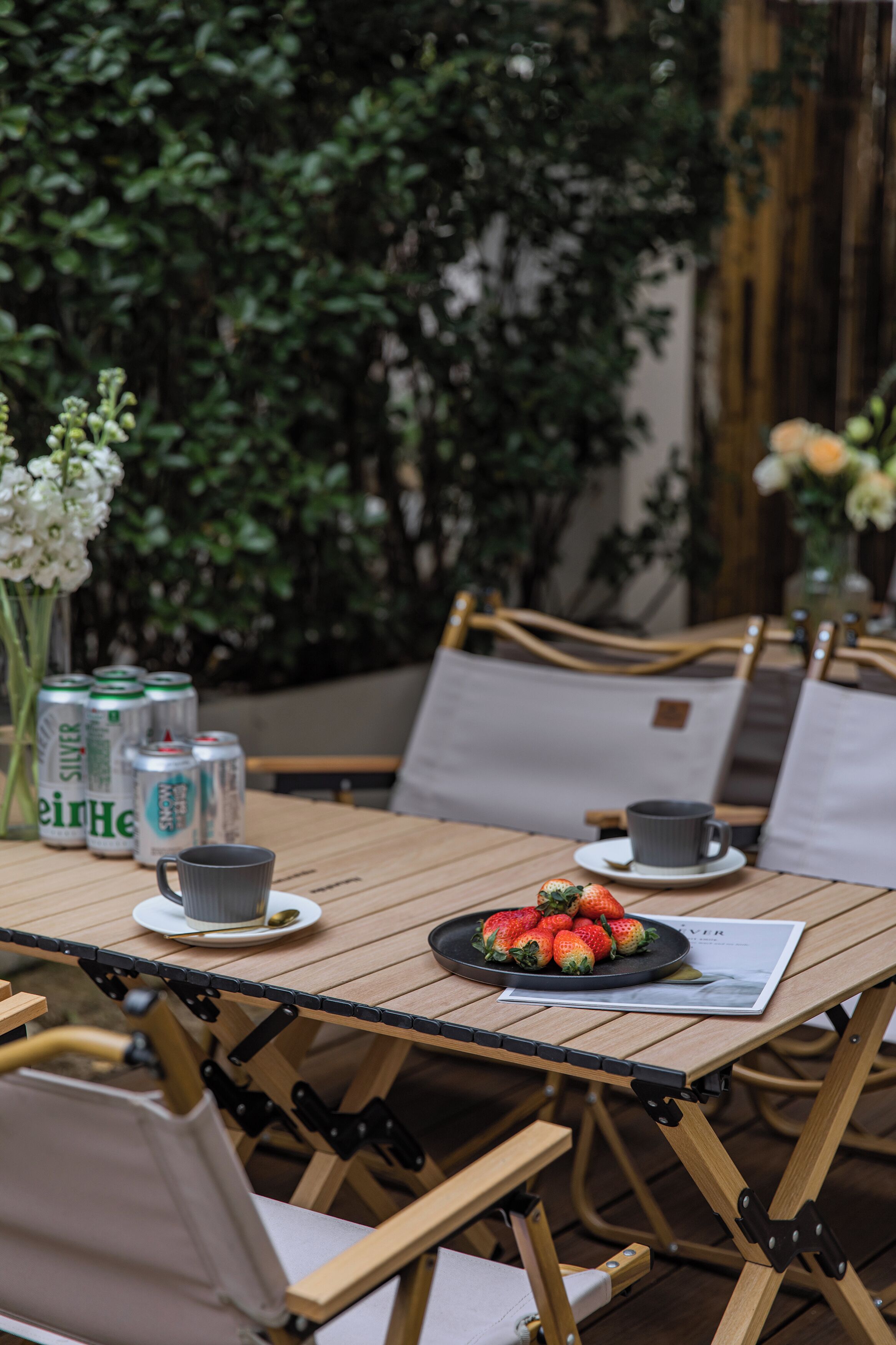 A wooden table with a plate of strawberries, a cup, and cans of beer.