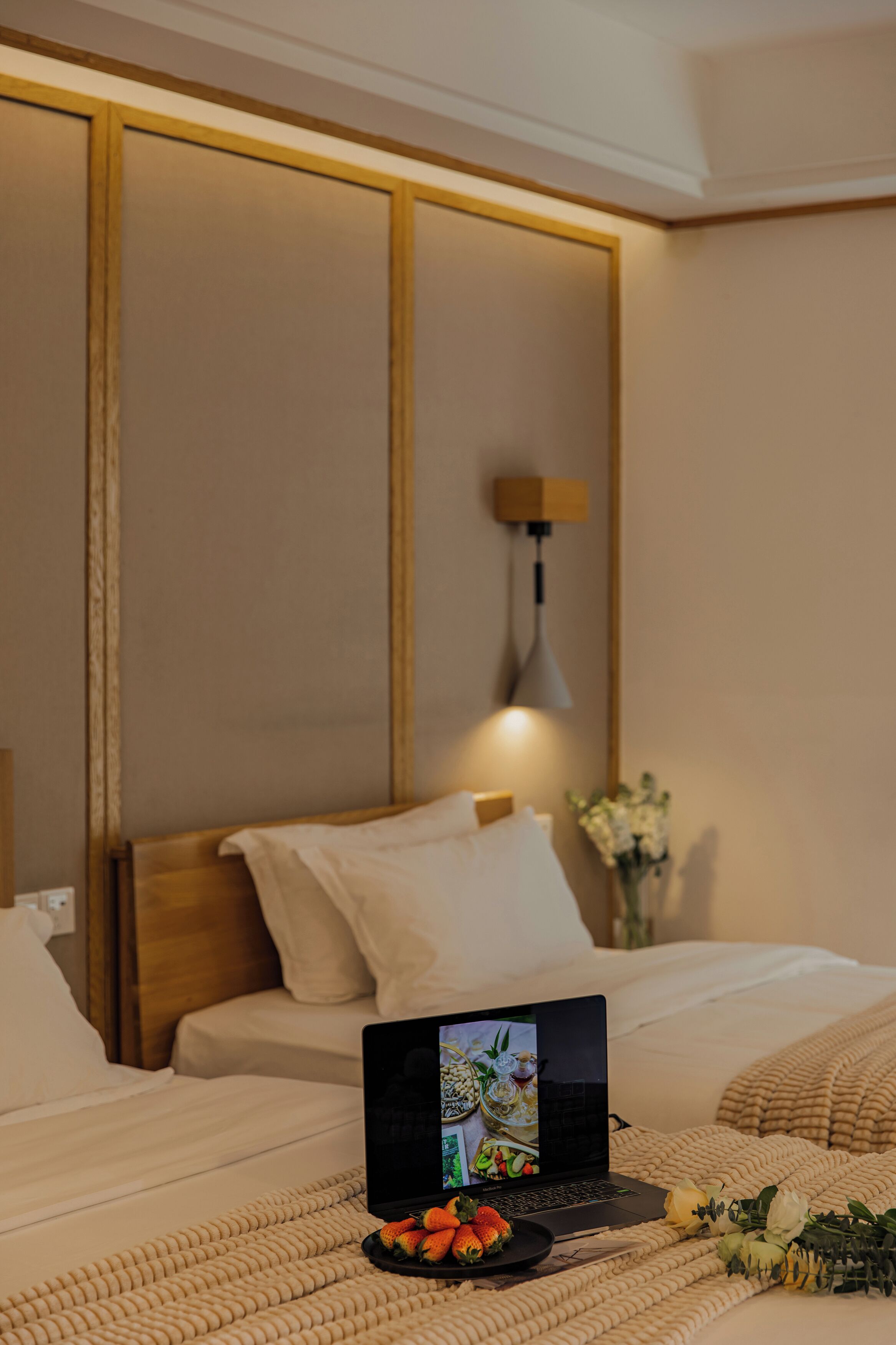 Una habitación de hotel con una cama, un ordenador portátil sobre la cama y una mesita con un plato de fresas.