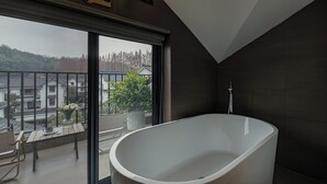A modern bathroom with a freestanding bathtub, a large window with a view of a residential area, and a balcony with a chair and potted plant. - Hangzhou West Lake Yueshang Yunshe Boutique Homestay (Hangzhou)