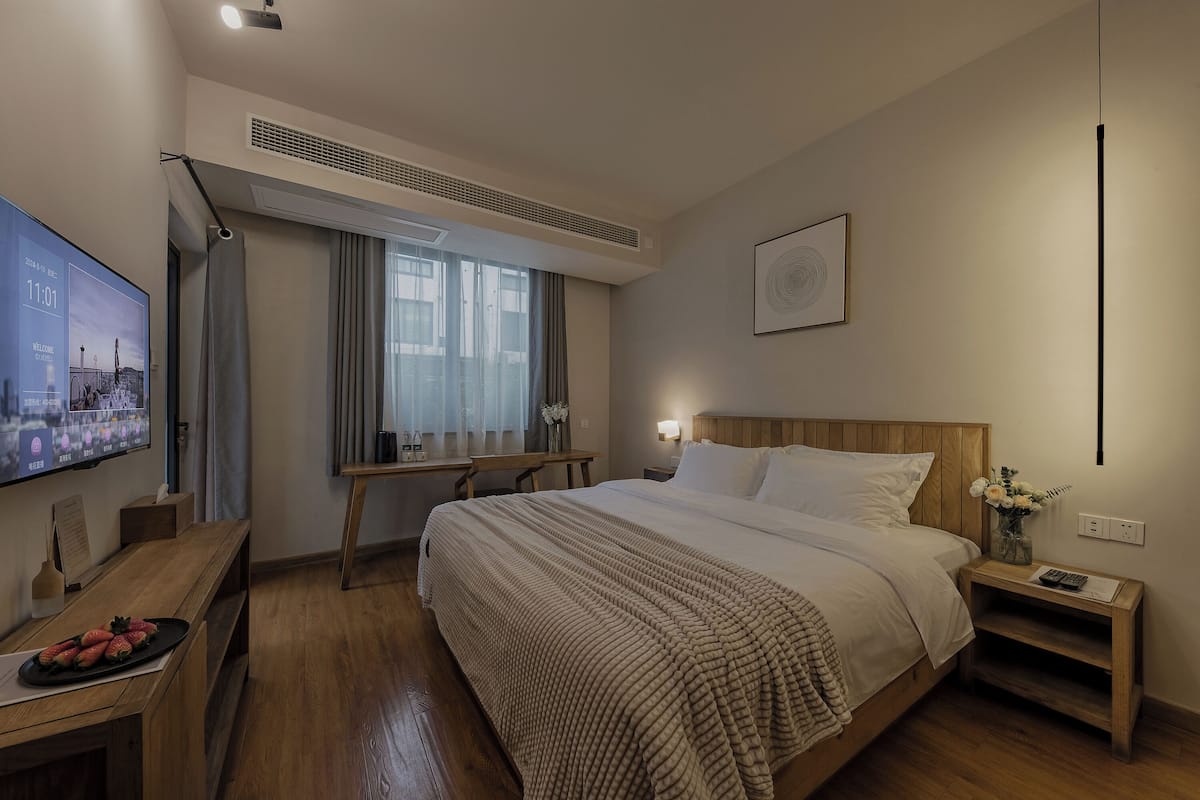 Ein Hotelzimmer mit einem großen Bett, einem Schreibtisch mit Flachbildfernseher, einem Nachttisch aus Holz und einem Fenster mit Vorhängen.