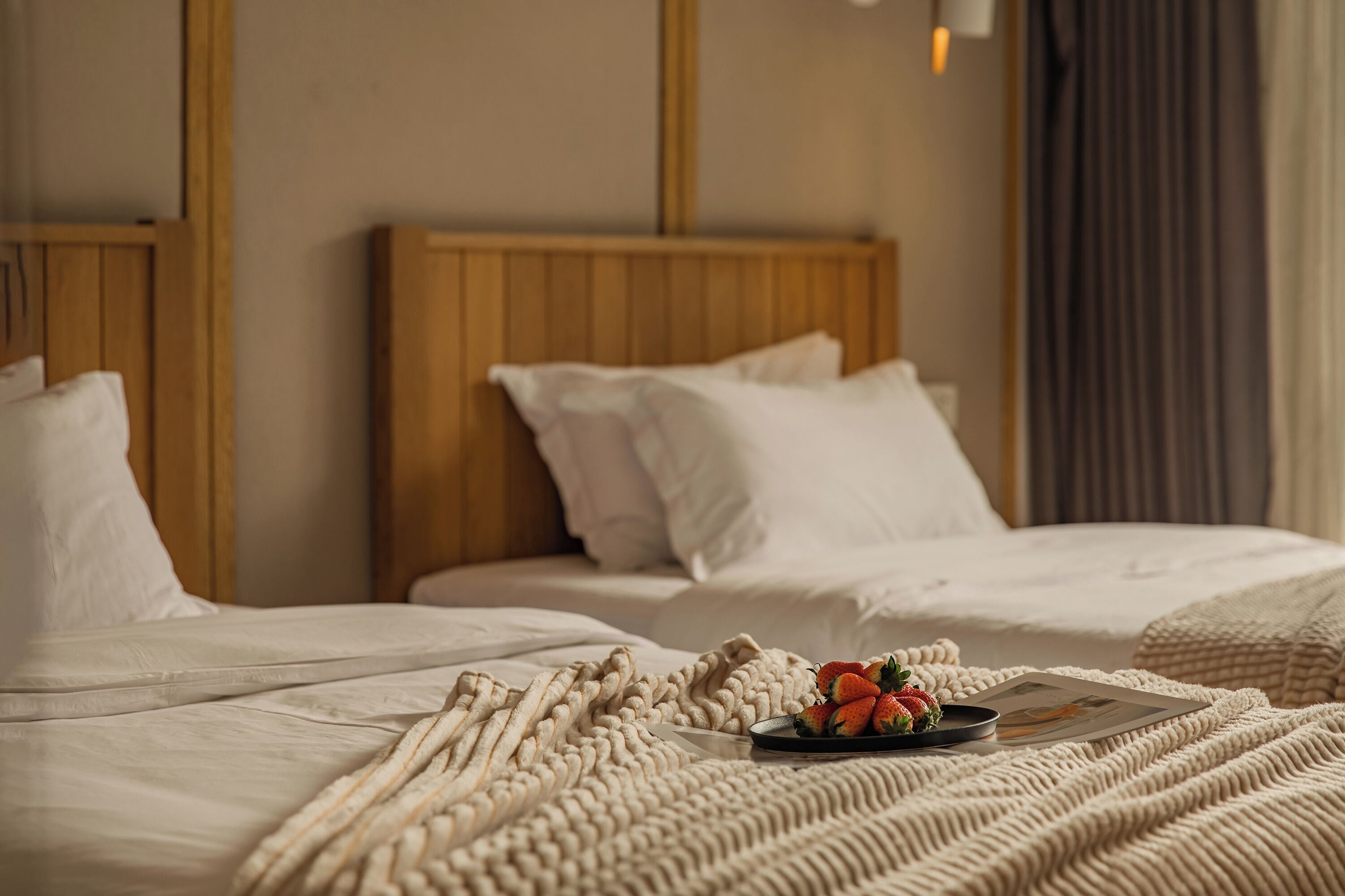 A hotel room with a wooden headboard, white bedding, and a plate of strawberries on the bed.