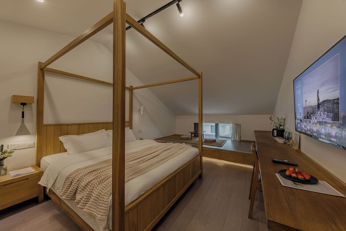 Ein Schlafzimmer mit einem Himmelbett, einem Schreibtisch mit einem Laptop und einem großen Fenster.