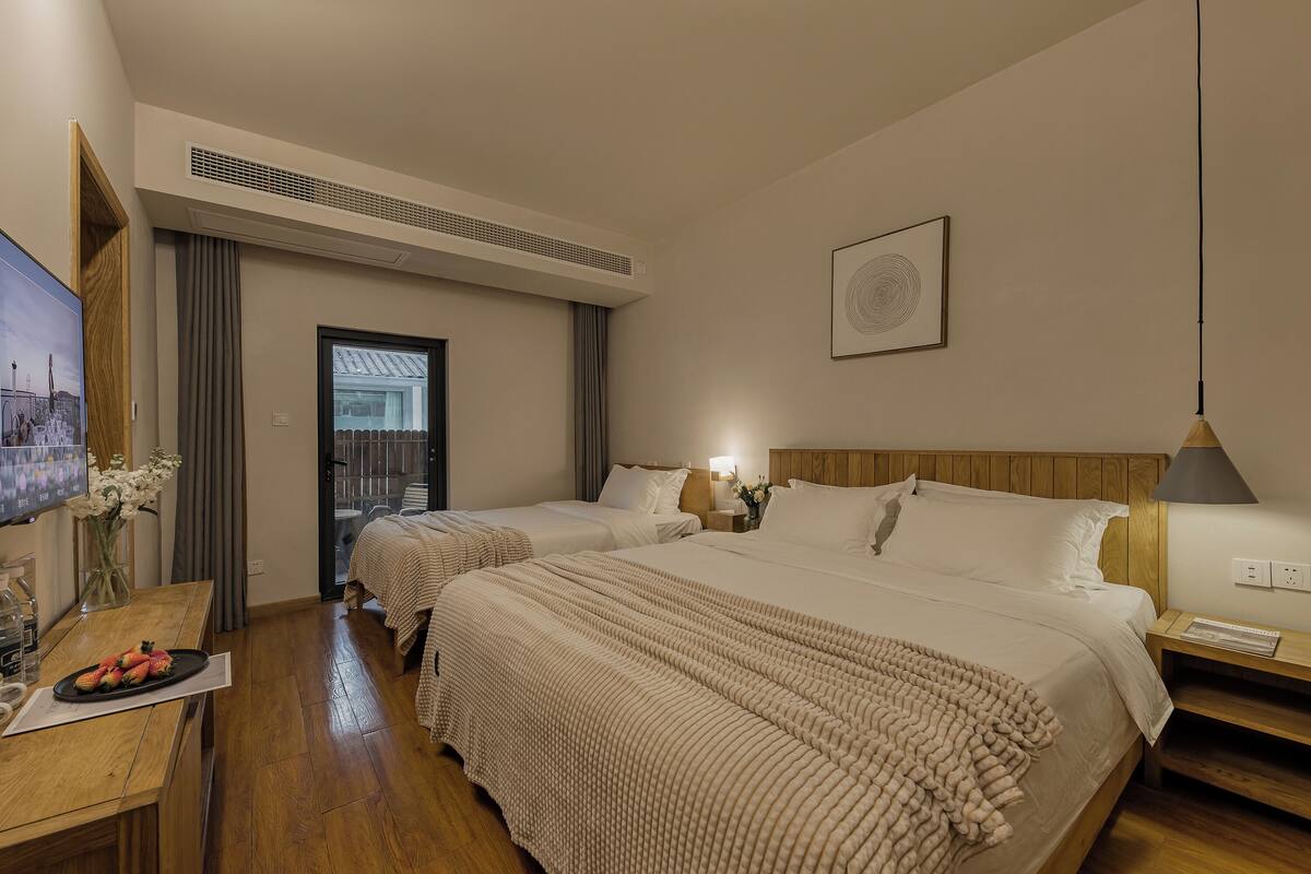 Ein Hotelzimmer mit zwei Betten, einem Holztisch, einem Fernseher und einem Fenster mit Vorhängen.