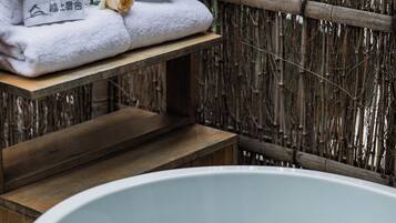 A spa area with a large bathtub, wooden shelves with towels, and a bamboo backdrop.