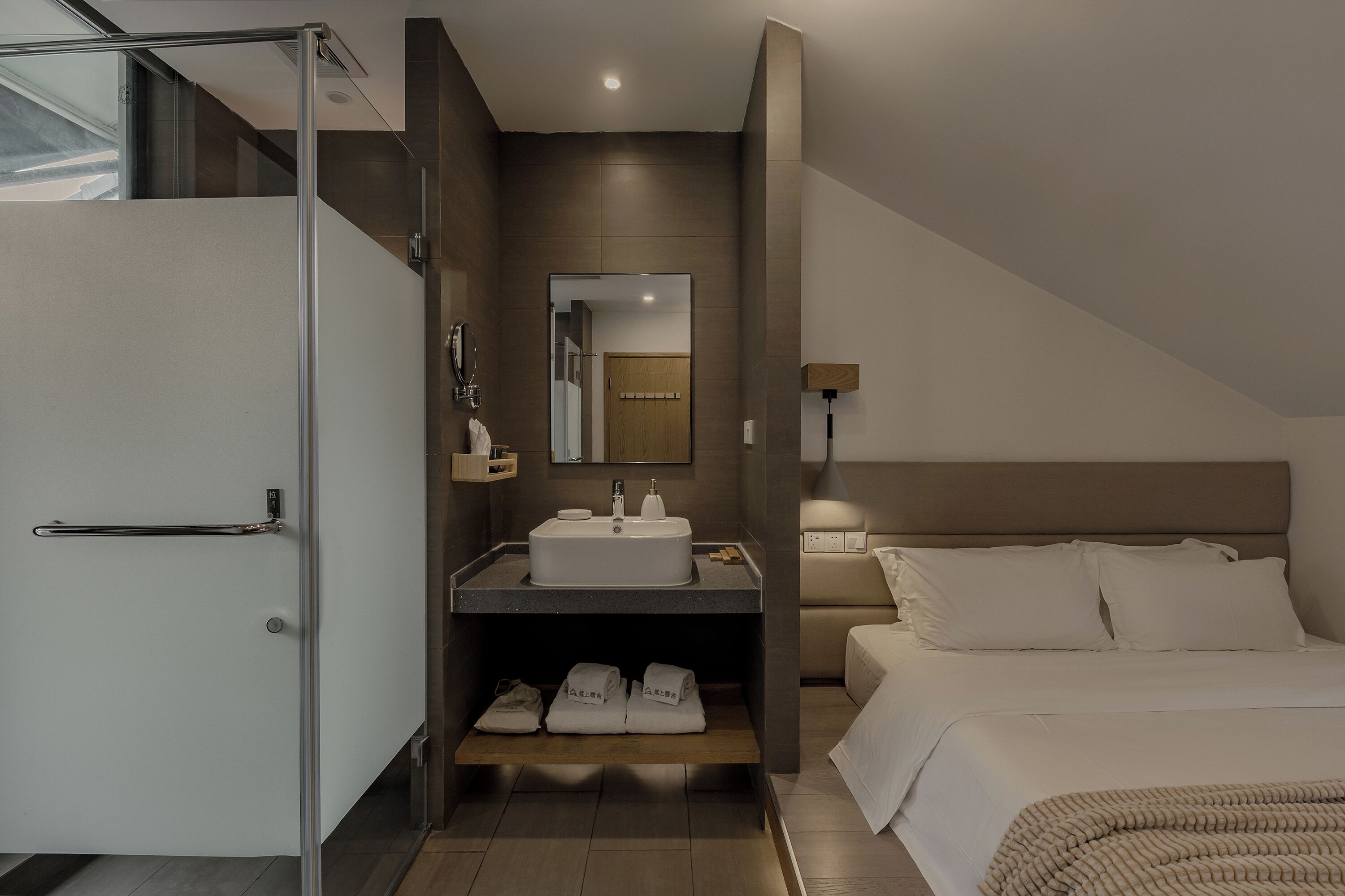 A modern hotel room with a shower, sink, and bed.