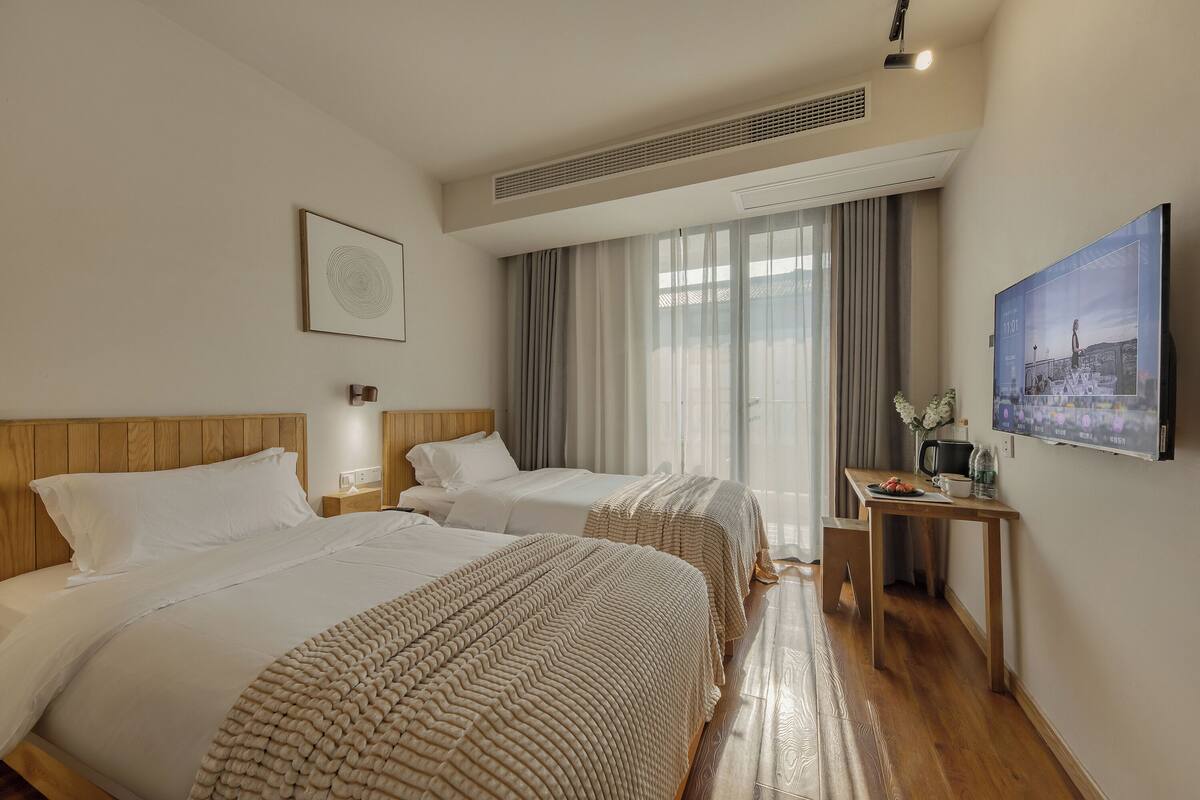 Ein Hotelzimmer mit zwei Betten, einem Schreibtisch und einem großen Fenster mit Vorhängen.