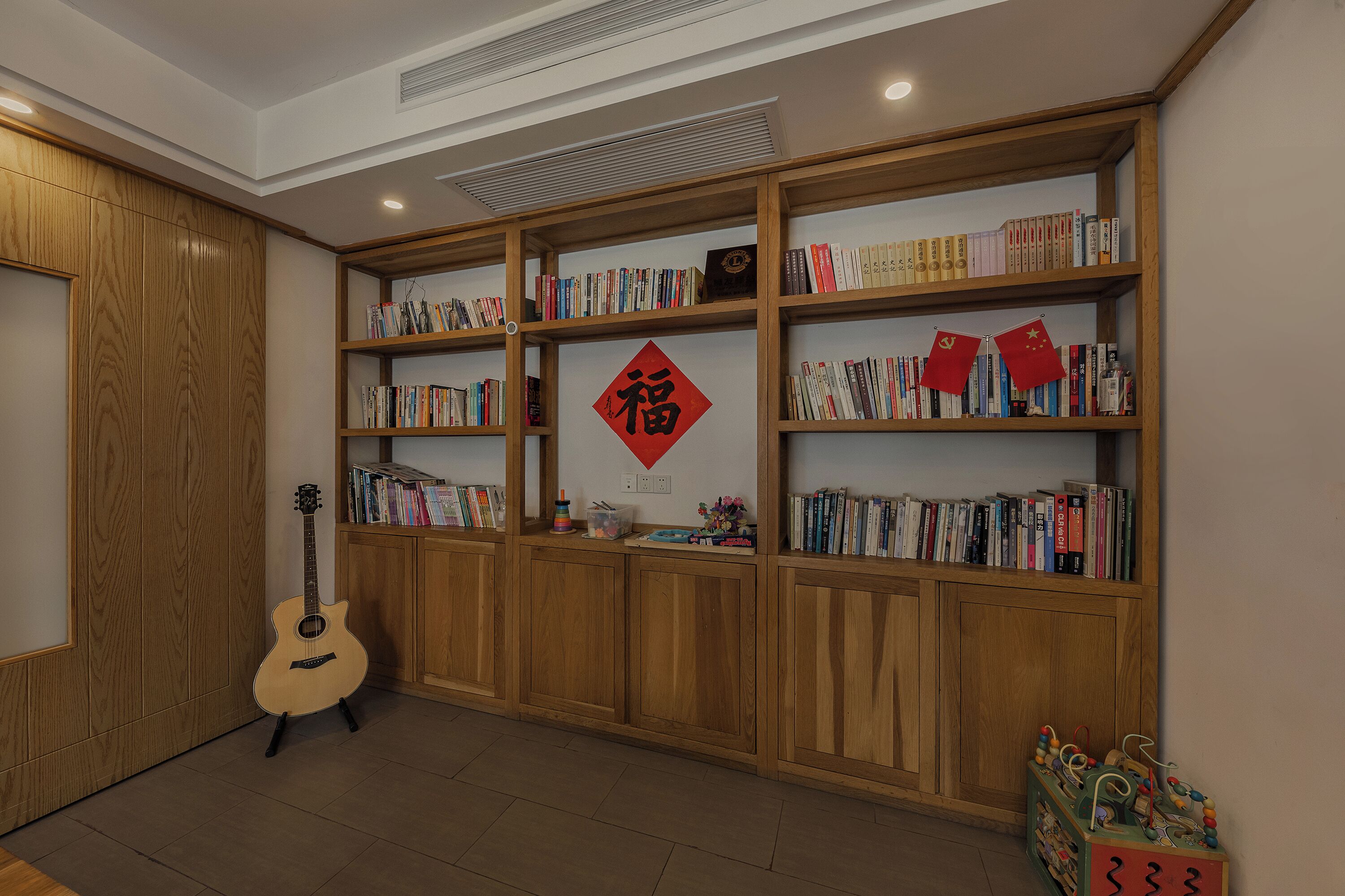 Een kamer met houten boekenkasten vol boeken en een gitaar.