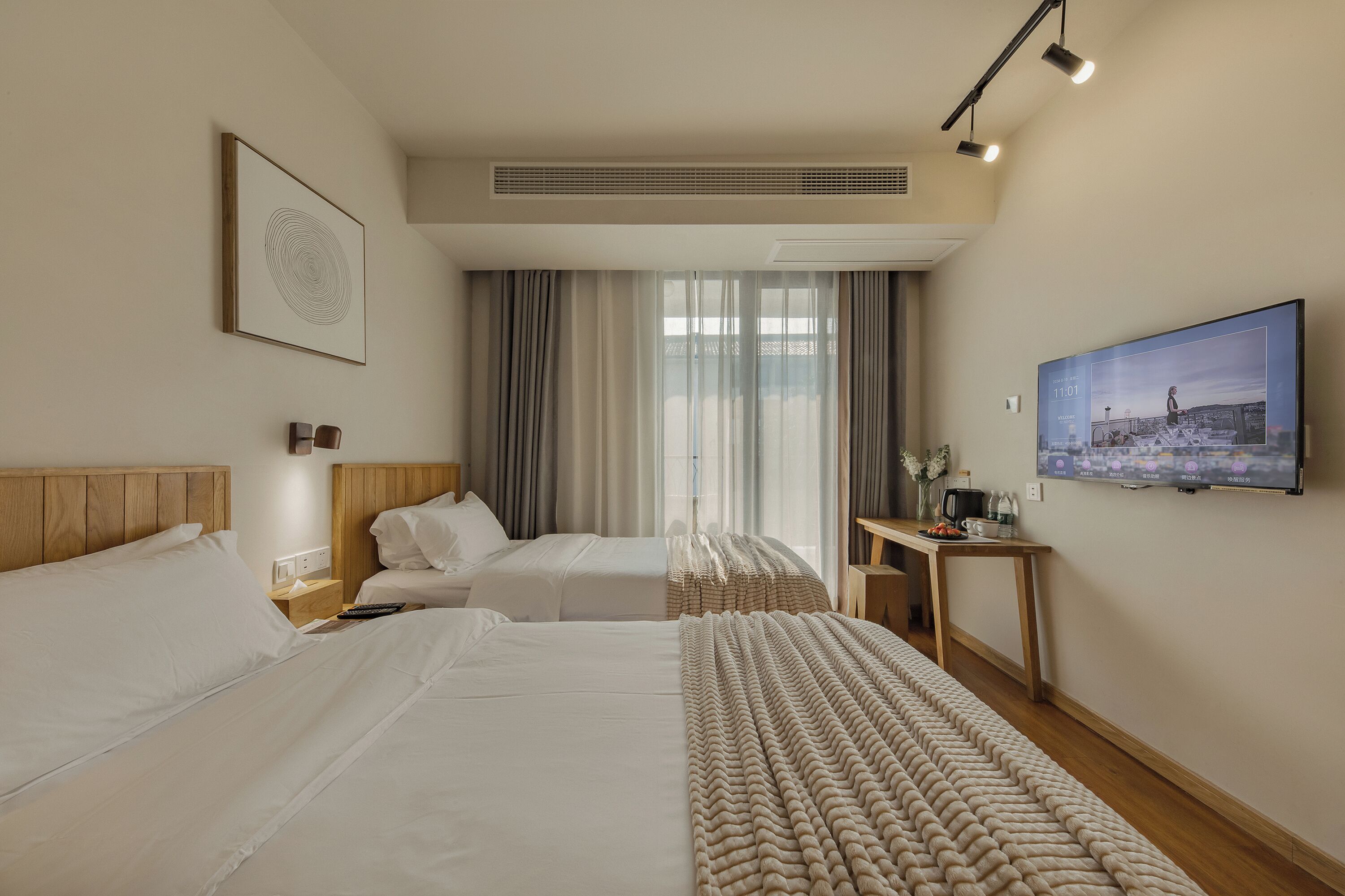 Een hotelkamer met twee bedden, een televisie, een bureau en een groot raam met gordijnen.