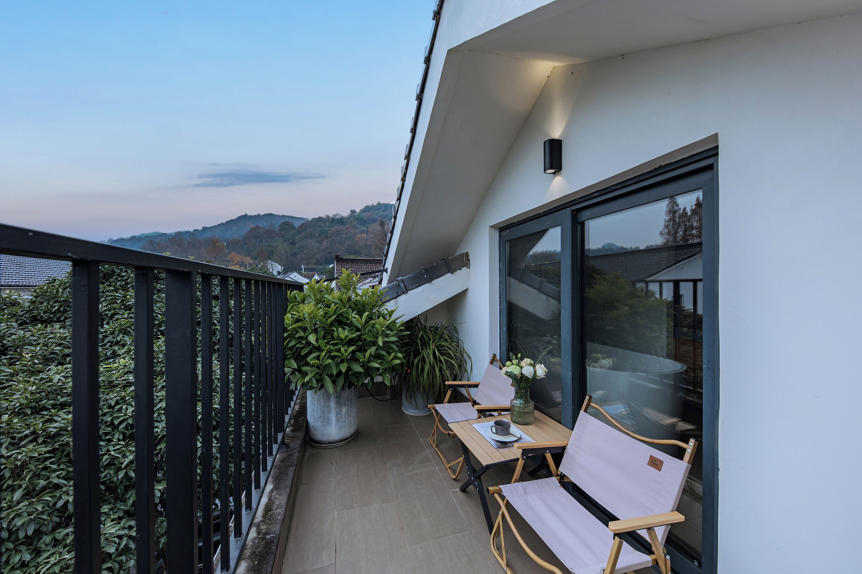 A balcony with a table and chairs, potted plants, and a view of the surrounding landscape.