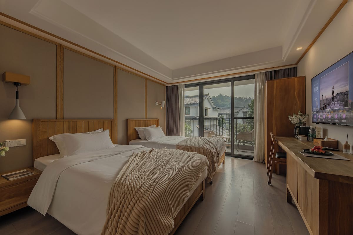 Ein Hotelzimmer mit zwei Betten, einem Holztisch und einem Balkon mit Blick auf traditionelle Gebäude.