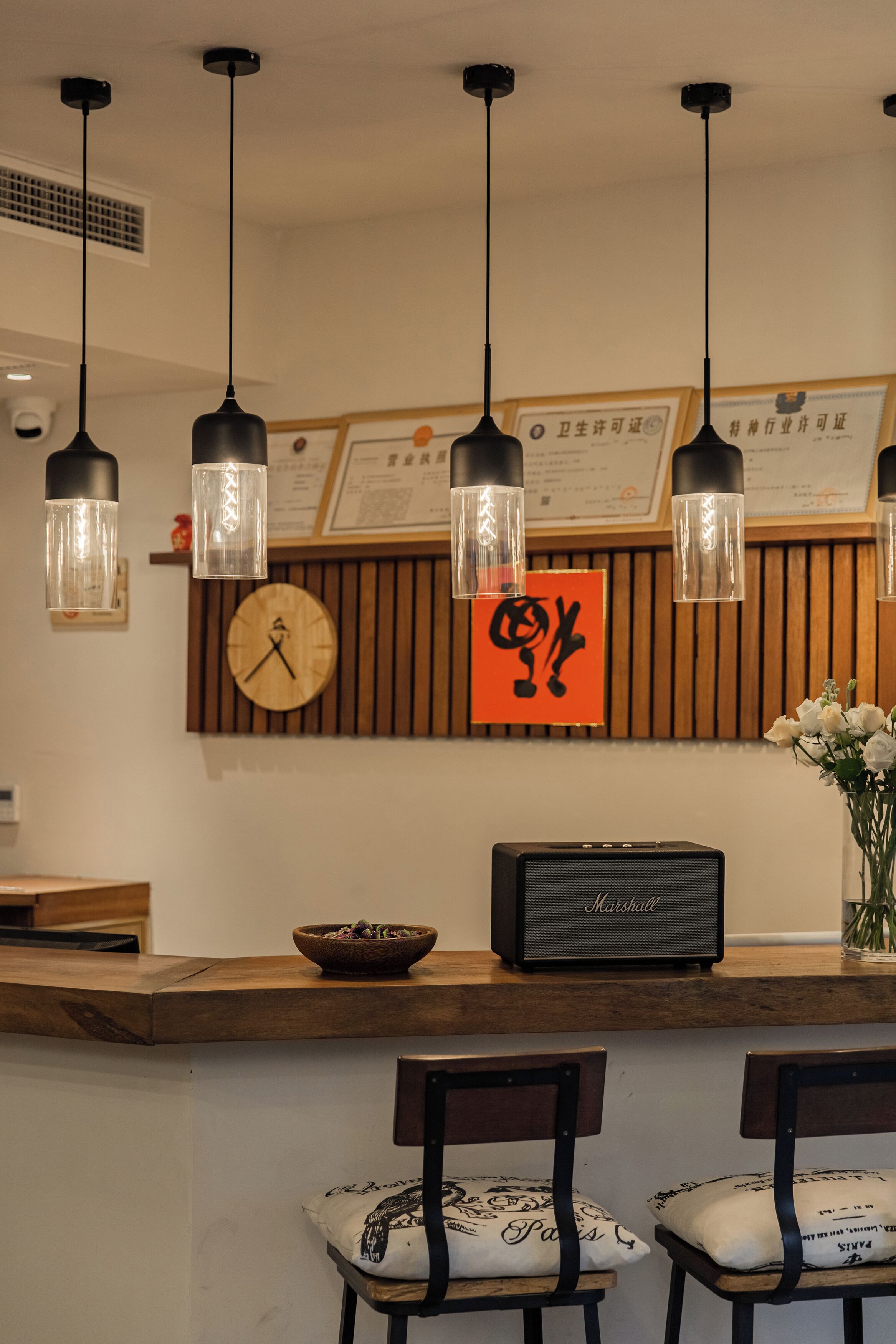 A reception area with a wooden counter, a clock, a framed certificate, a Marshall speaker, and two chairs with patterned cushions.