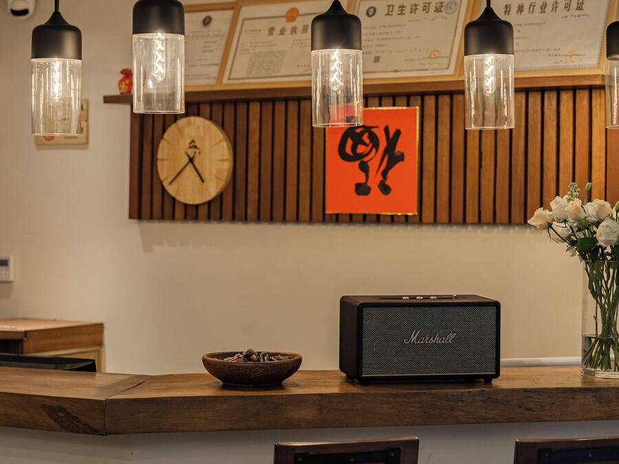 Un espace d’accueil comprenant un comptoir en bois, une horloge, un certificat encadré, un haut-parleur Marshall et deux chaises dotées de coussins à motifs.