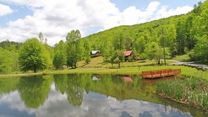 A serene lakeside setting with a wooden dock, lush greenery, and a small building in the background.