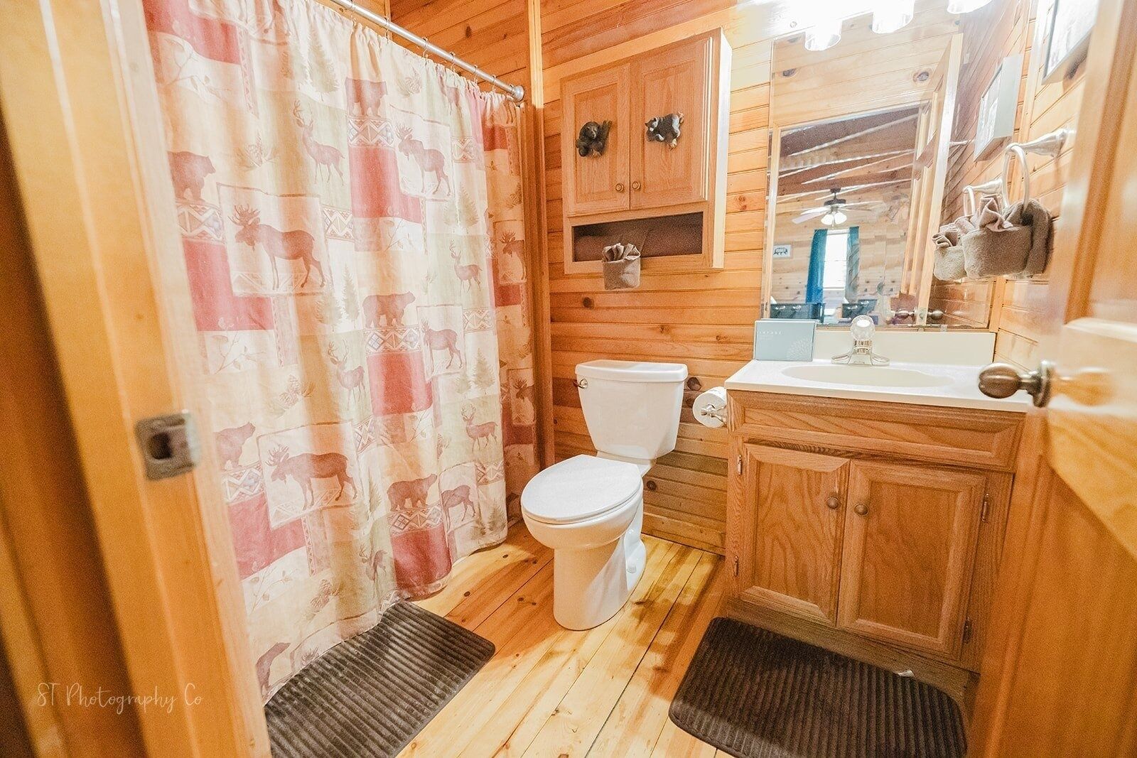 Une salle de bain rustique, aménagée dans une cabane en bois, avec des toilettes, un lavabo et un rideau de douche orné de motifs animaliers.