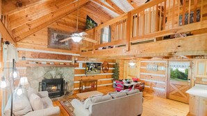 A cabin interior with a fireplace, wooden walls, a ceiling fan, and a 'Welcome to the Cabin' sign.