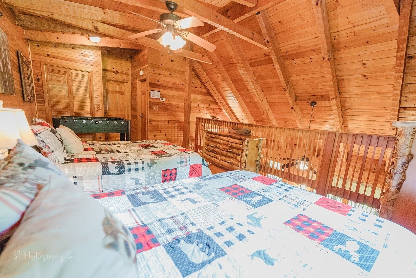 A cozy log cabin bedroom with a large bed, a wooden ceiling fan, and a rustic wooden railing.