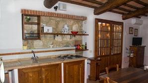 A kitchen with a stone backsplash, wooden cabinets, a gas stove, and a dining area with a wooden table and chairs. - La Canonica (Montalcino)
