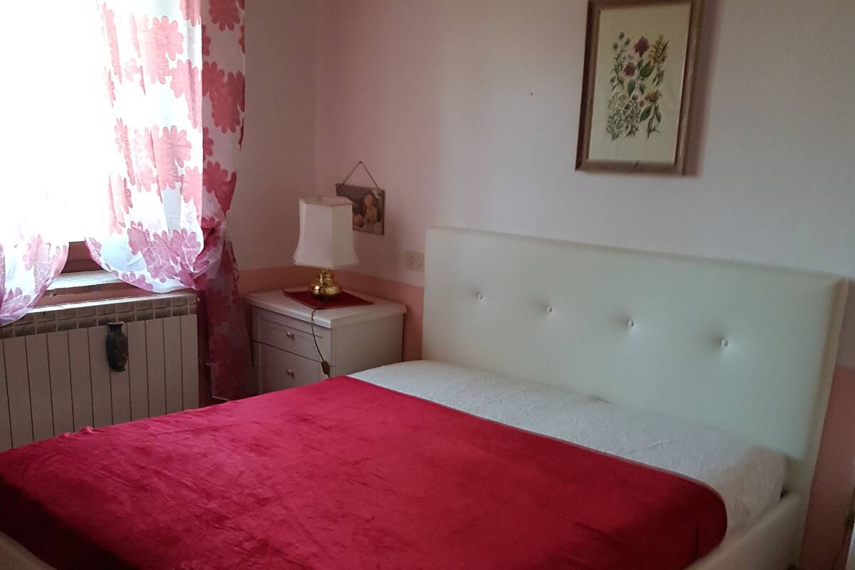 A bedroom with a bed, a nightstand, a lamp, a framed picture on the wall, and a window with curtains.
