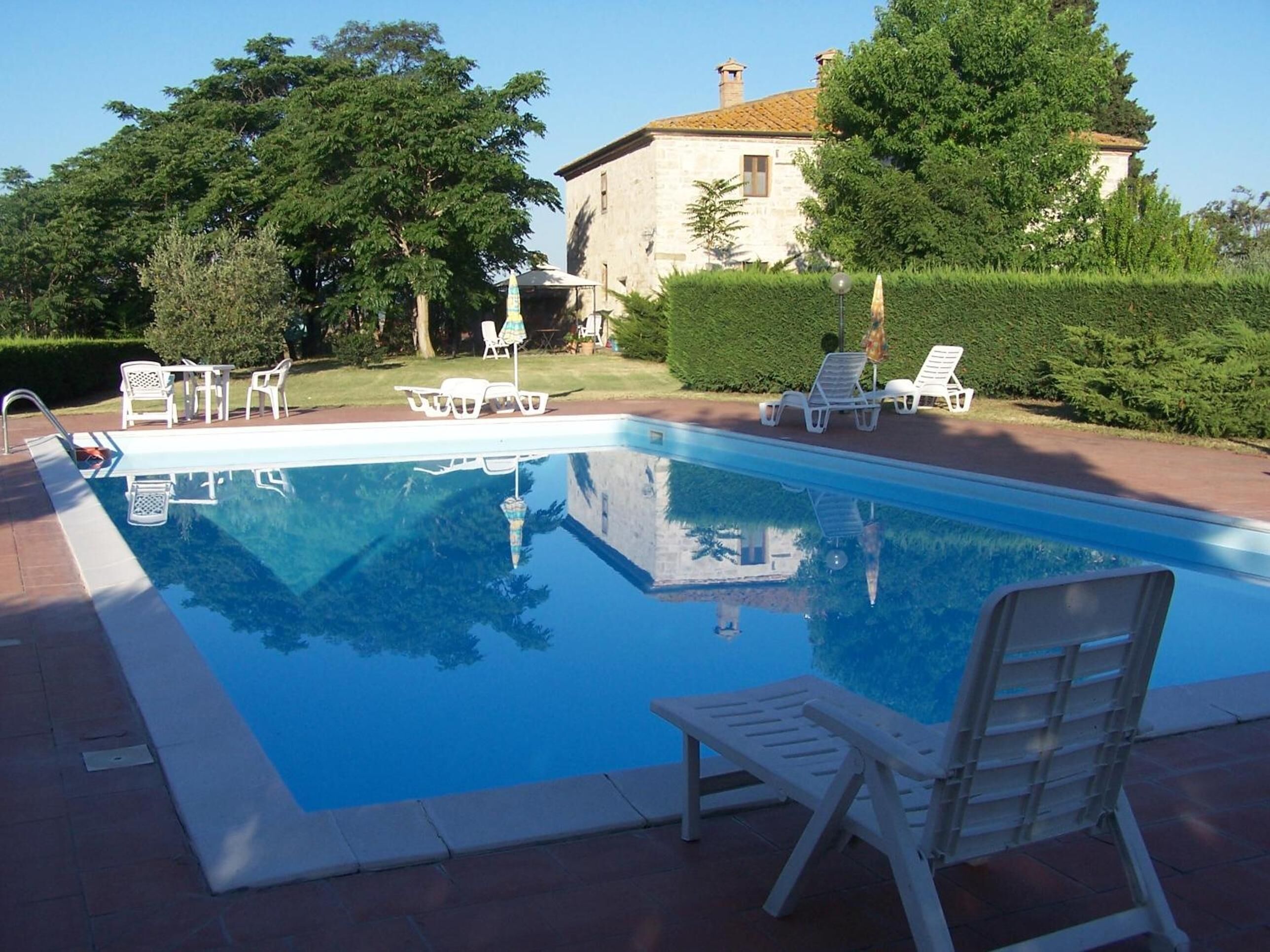 A rectangular swimming pool with clear blue water, surrounded by white lounge chairs and a brick patio.